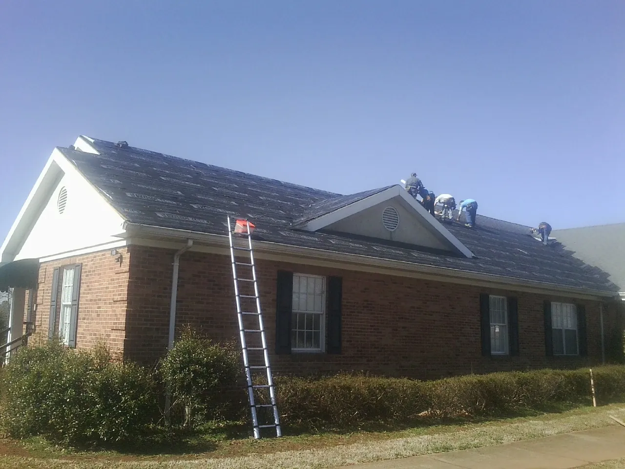 Crew tearing shingles off a brick ranch roof with a ladder set — Emergency Roof Repair work by our crew in The Plains