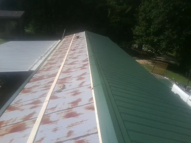 Old rusted panels beside newly installed green metal roofing — Wind Damage Roof Repair by Roofing Brothers in The Plains